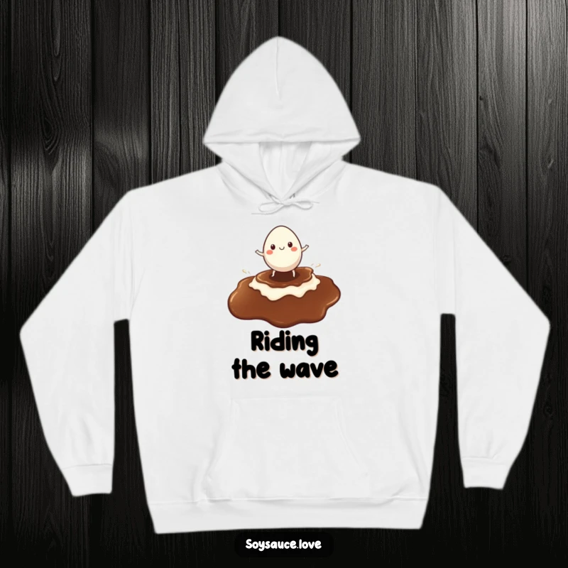 Funny hoodie featuring a cheerful egg character riding a giant soy sauce puddle like a surfboard, radiating fun.
